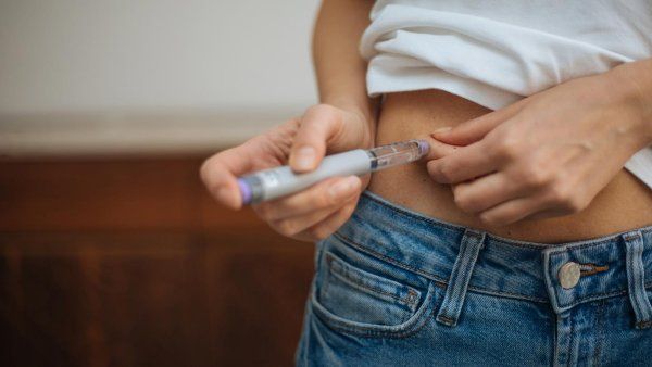 A woman lifts her shirt to inject a weight loss drug into her abdomen.