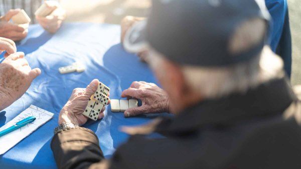 A group of elderly people sitting together at a table and playing dominos.