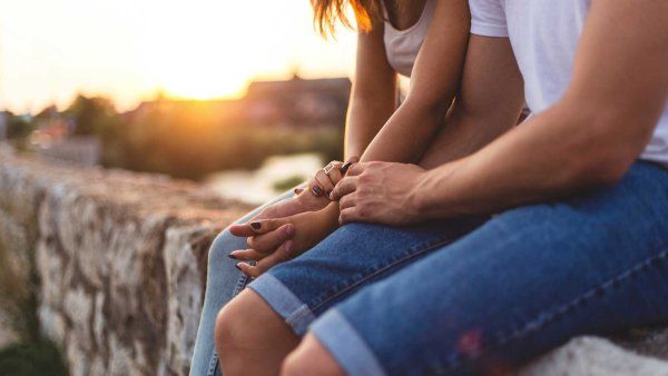 A young teen couple holds hands while they sit together.