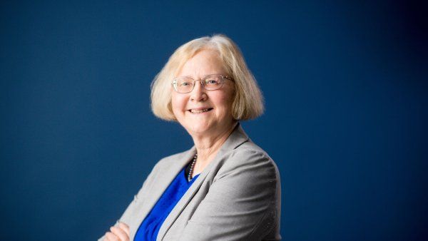 Elizabeth Blackburn smiles while wearing a suit jacket in front of a blue wall.