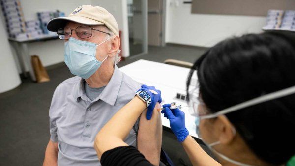 An elderly man wearing a mask receives a vaccine from a medical professional.