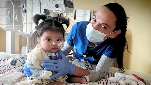 Baby surrounded by toys is cared for by nurse.