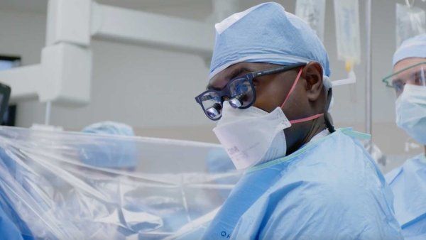 Neuroseurgon Shawn Hervey-Jumper wears surgical scrubs and a mask, along with surgical loupes, while he performs neurosurgery.