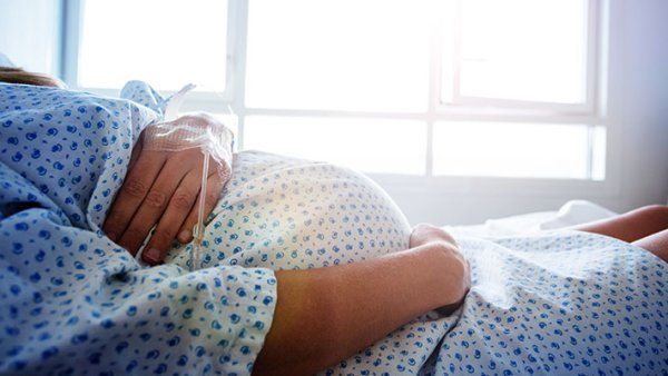 Close-up of a pregnant woman's belly in the hospital bed with catheter in hand