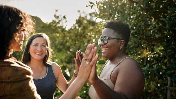 A group of women laughing and exercising, standing with their hands together