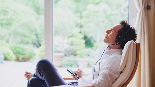 A man wearing headphones and office attire relaxes and meditates on a chair.