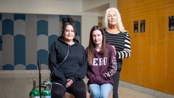 Two sisters, one of whom uses an oxygen tank to breathe due to the COPA disease, stand with their mother Betty.