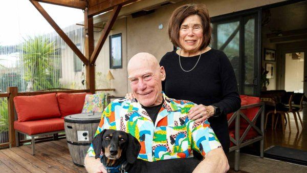 Gary Seifer smiles as he holds his dog and sits in front of his wife.