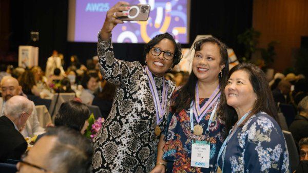 Three women in a banquet hall take a selfie at the 2025 Alumni Achievement Awards even.t