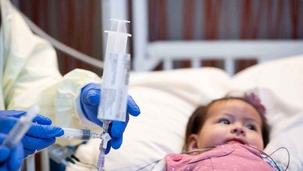 A baby is given medication through an IV by a medical professional wearing protective gear.