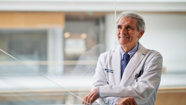 Stephen Hauser looks up and smiles in a doctor’s white coat inside the UCSF Weill Institute for Neurosciences building.
