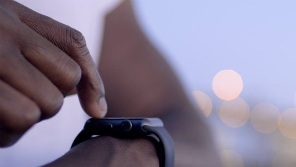 wrist-focused view of a person wearing a tank top adjusting a smart fitness tracking watch
