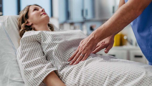 Woman reclining on medical bed, doctor palpating woman's abdomen, using hands and steady pressure.