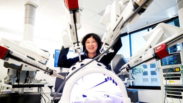 Dr. Hueylan Chern smiles as she stands with a surgical robot that has multiple arms.