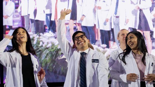 Excites students in white coats wave with pride on stage.