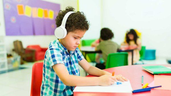A young boy wears headphones inside a kindergarten classroom.