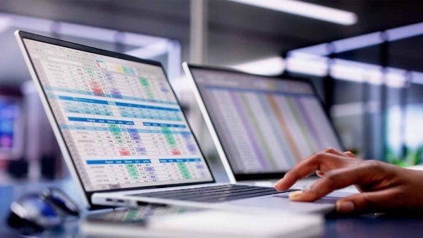 A hand is seen scrolling spreadsheets in an office.