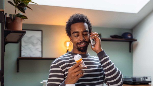 A young Black man receives telehealth care as he looks at his medications.