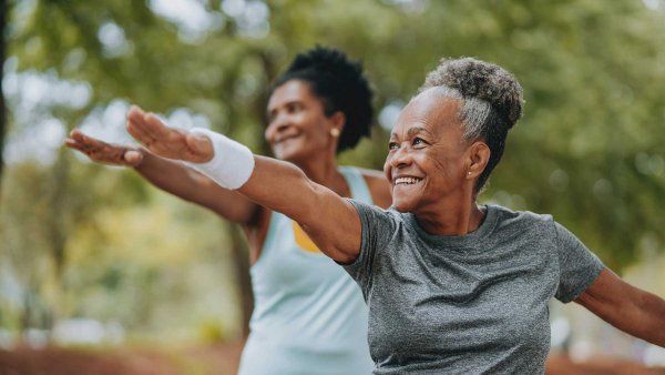 Two Black senior-aged women smile as they do exercise outdoors.