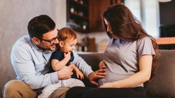 Man with glasses and his son touch smiling pregnant woman's belly.