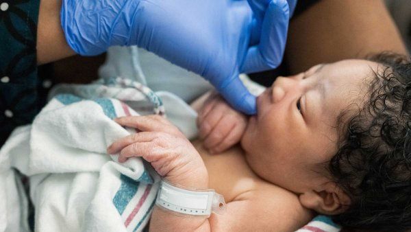 A nurse wearing a blue latex glove holds a newborn baby boy.