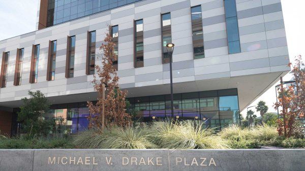 A low concrete wall in an outdoor plaza with embedded letters that read "Michael V. Drake Plaza."