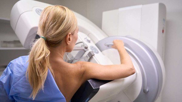 A woman stands at a mammogram machine.