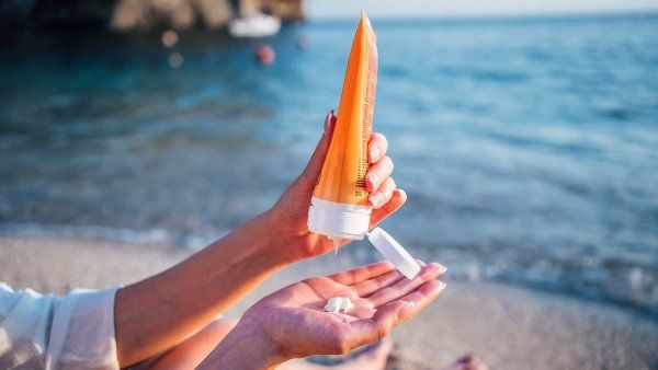 A woman applies sunscreen while sitting on a beach.