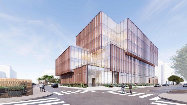 Rendering of the U C S F Bakar Ear and Hearing Institute, a contemporary research building with stacked, offset volumes and a glass curtain wall wrapped in vertical copper-toned fins, situated on a sunny urban corner in Mission Bay with crosswalks, cars, and pedestrians.