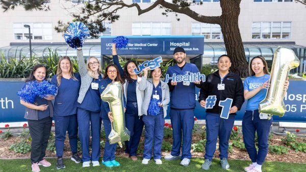 Medical professionals wearing medical scrubs cheer and hold balloons and pom poms outisde of the U C S F Medical Center at Parnassus Heights.