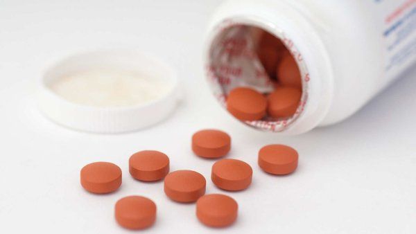 Close-up of a white prescription pill bottle with a blue and white capsule resting on the label and other pills scattered in the background.
