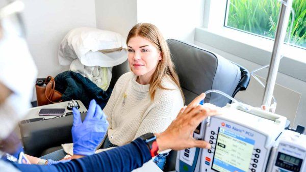 A young 30-year-old patient named Megan smiles as she is assisted by a medical professional while receiving an infusion to treat colorectal cancer.