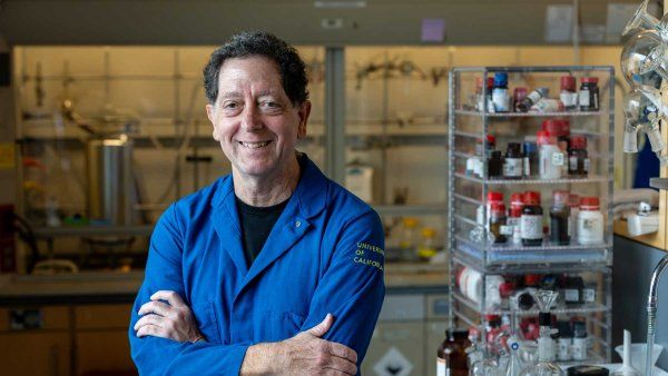 Kevan Shokat wears a blue lab coat as he stands in his lab at U C S F.