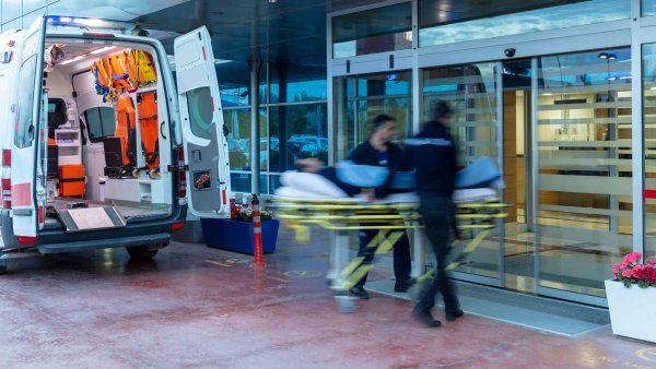 Paramedics rush in to carry a person on a stretcher from an ambulance into an emergency department.