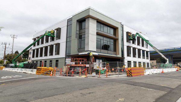 An exterior shot of construction of Temescal Hall with construction workers on cranes.