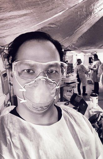 Portrait of Kenny Banh in an N95 mask and goggles, inside a tent.