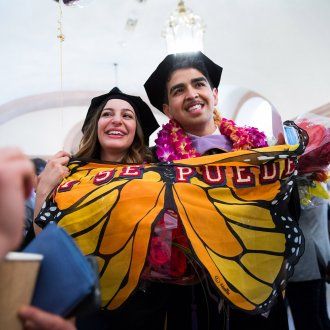 Two graduates hold up a flag of butterfly wings that reads Si Se Puede