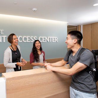 Two workers at the Student Success Center laugh with a patron at the welcome desk