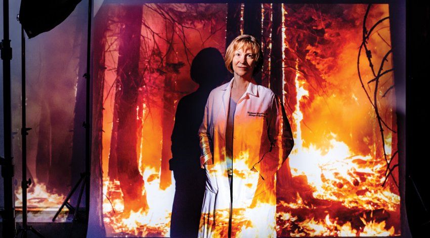 Portrait of Dr. Katherine Gundling in a photo studio setting with a projection of a forest fire.