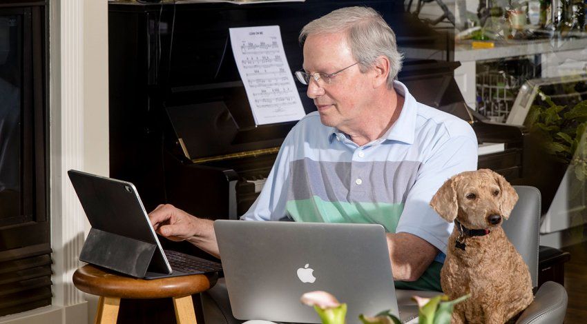 Robert Wachter, MD, sitting in his home, working on a tablet, with a computer in his lap, and his dog by his side.