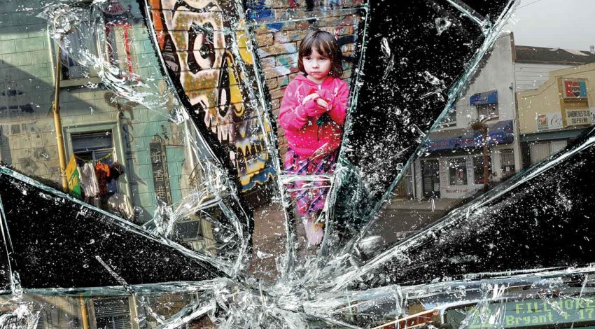Photo collage with broken glass: run down buildings and a small child in front of a graffitied wall.