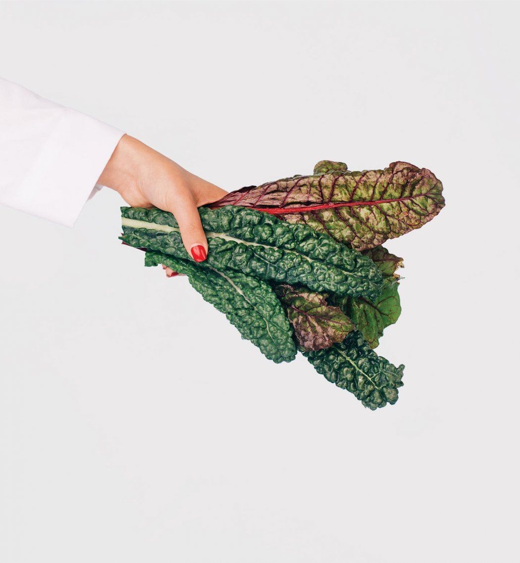 Photo of a hand in a doctor's white coat holding a bunch of chard.