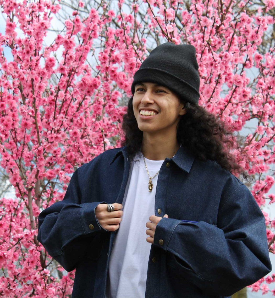 Anthony Orosco adjusts his jacket and stands in front of cherry blossom trees.