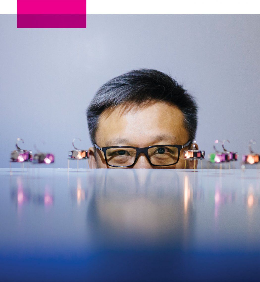 Wendell Lim peaks up from behind a table that holds small robots.