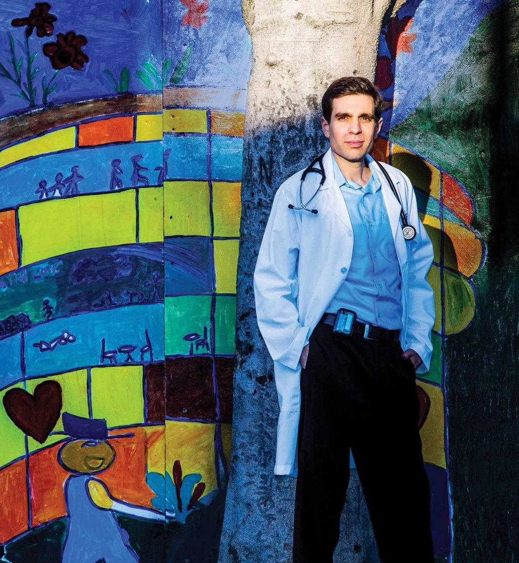 Jonathan Van Nuys stands in front of a colorful mural in a lab coat with stethoscope.