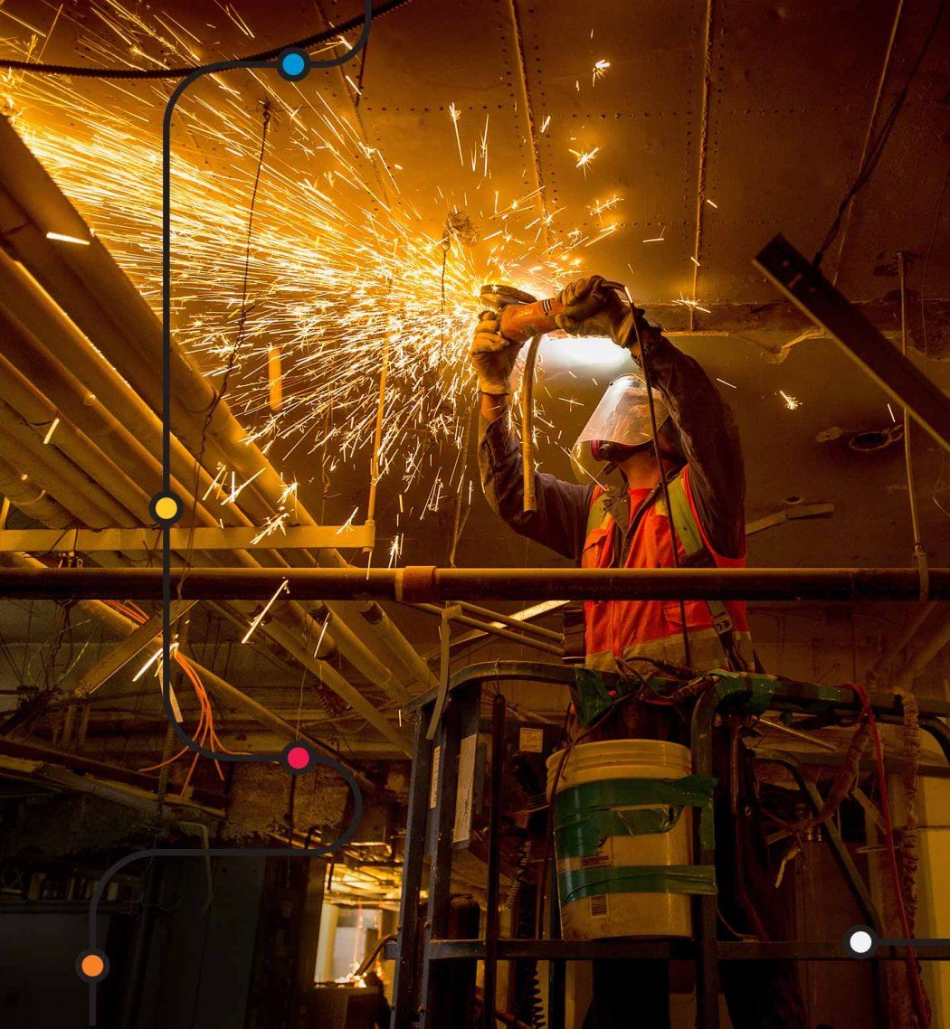 Sparks fly as a construction worker uses a saw against metal pipes in a building.