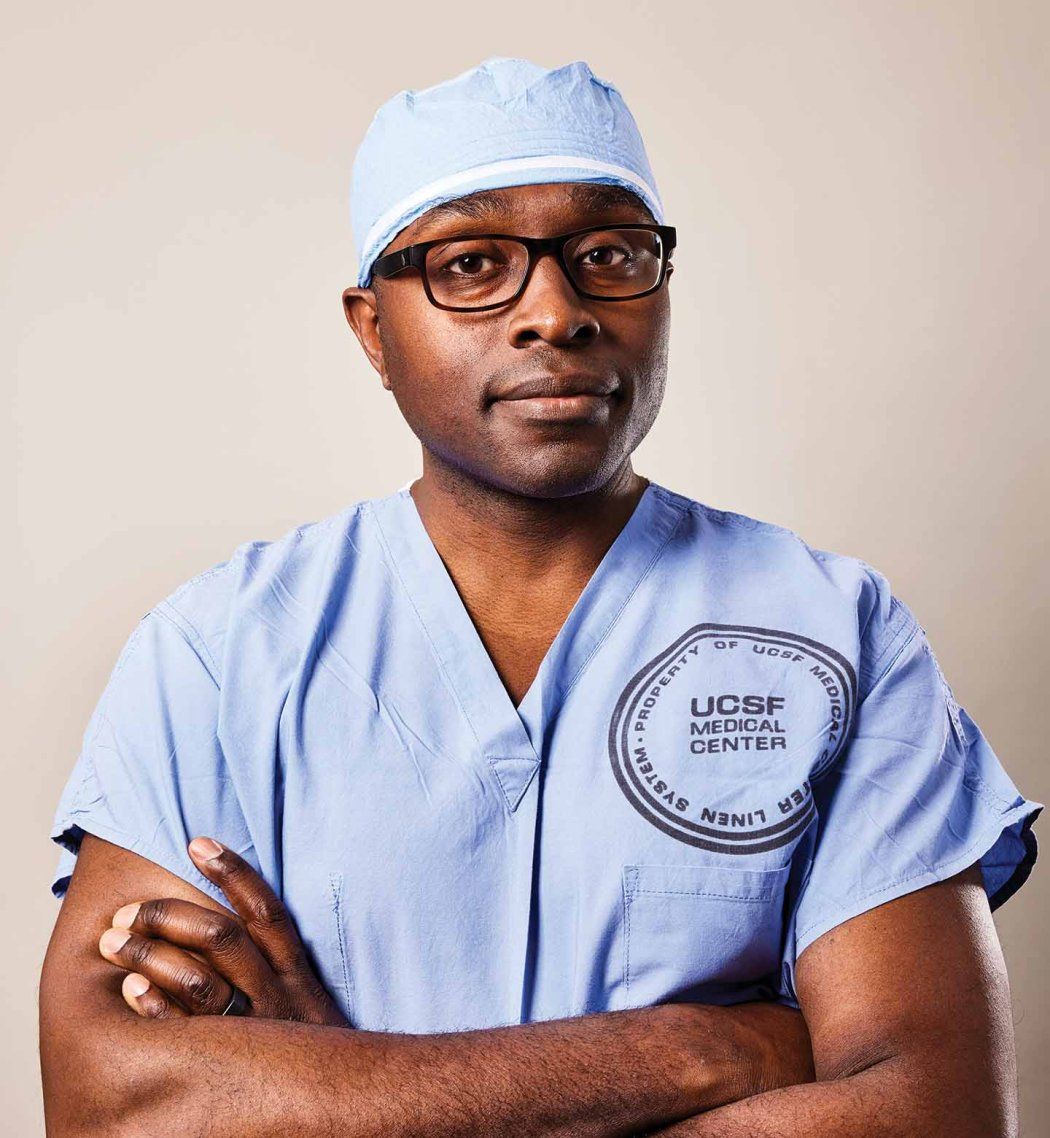 Portrait of neurosurgeon Shawn Hervey-Jumper, standing with his arms crossed in blue surgical scrubs.