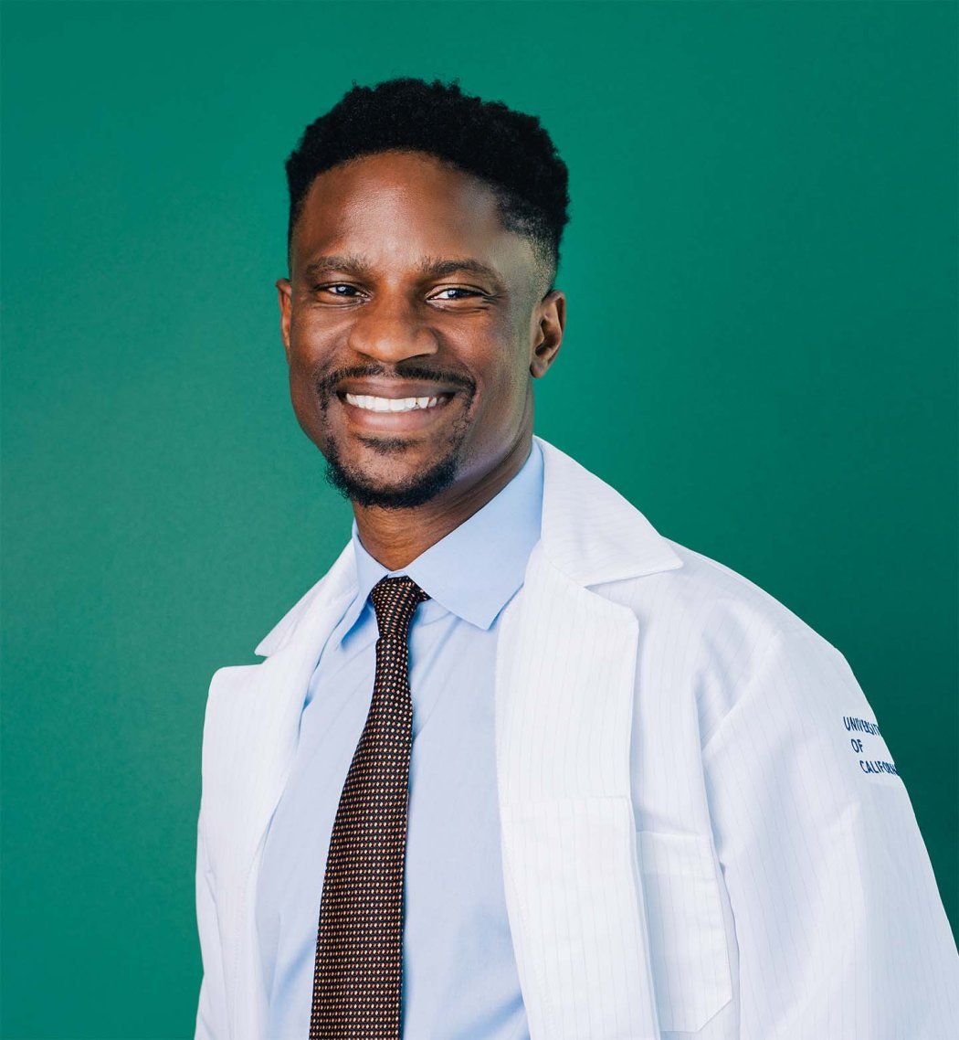 Akinyemi Oni-Orisan wearing a white lab coat and a brown tie.
