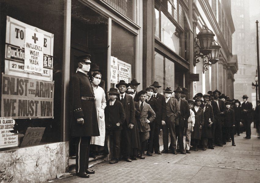 Line of people waiting for flu masks at 30 Montgomery Street, San Francisco, 1918. The man in uniform and the nurse in the doorway are wearing masks, as are a few of those in line. A sign on the window bearing the Red Cross logo reads: “Influenza. Wear Your Mask.” A sign underneath reads: “Enlist in the Army. We Must Win.”