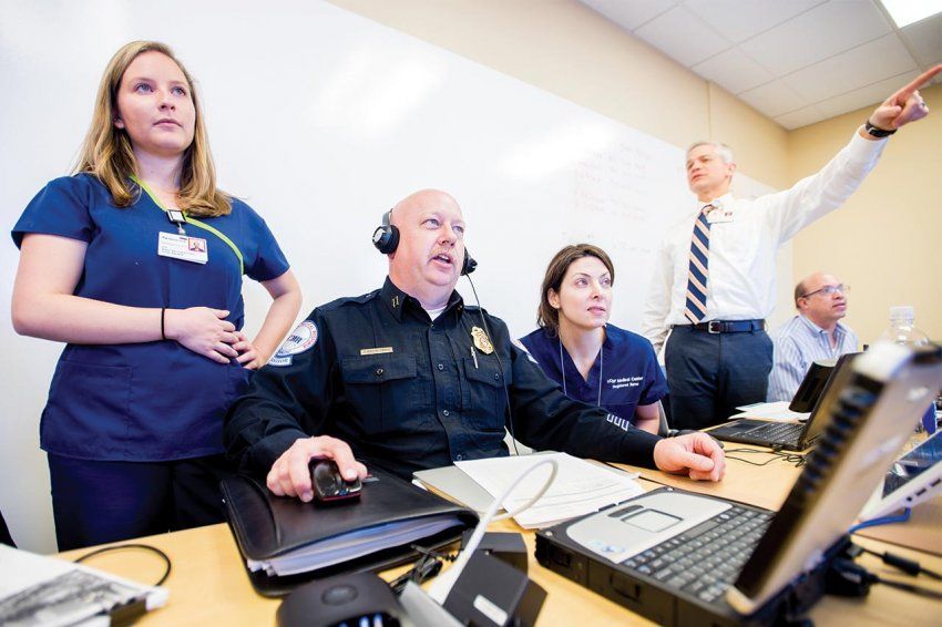 A police officer and UCSF staff sit and stand behind a command table with phones and computers.